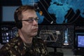 An elderly military man with headphones looks at the monitor against the background of a world map in the military center. Concept Royalty Free Stock Photo