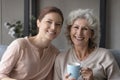 Elderly mother grown daughter sit on couch drink coffee talk