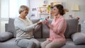 Elderly mum giving present to daughter sitting sofa at home, relations closeness