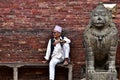 An elderly Nepali man sitting next to a statue in Kathmandu
