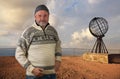 A Norwegian with a beard and a typical sweater stands in front of the iron globe at the North Cape.