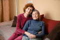 Elderly old cute woman with Alzheimer`s very happy and smiling when eldest daughter hugs and takes care of her, at home on sofa. Royalty Free Stock Photo