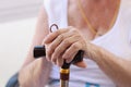 Elderly pensioner holding hands on wooden cane closeup