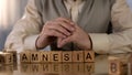 Elderly pensioner making word amnesia of wooden cubes on table, health care