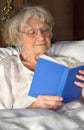 Elderly pensioner reading a book in bed Royalty Free Stock Photo