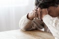 Elderly person in melancholy praying with rosary