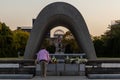 Elderly person putting flowers in front of the Hiroshima Peace Memorial at sunset