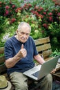 Elderly person works on a laptop and enjoys life, smiling happily. An old man with a mustache gestures that everything is in order