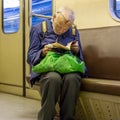 Elderly, poor, lonely man in broken glasses enthusiastically reading a tattered book