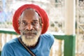 Elderly rasta man wears a red rasta hat which hides his long grey dreadlocks