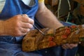 Elderly repairman painting with paintbrush on a small business a woodwork. Senior artisan with big hand painting artwork.