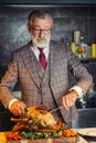 Old-aged handsome man in formal expensive suit cutting out roasted chicken