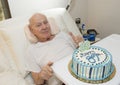Elderly retired family physician with a thumbs up signal for his 89th birthday cake delivered to his bedside.