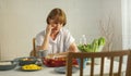 Elderly retired grandmother stay at home with unhappy face sitting alone on eating table in house. Depressed mature Senior old Royalty Free Stock Photo