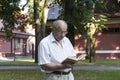 An elderly retired man walks alone in the park. An old, balding man with glasses stands against the background of a red building