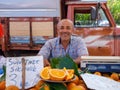Elderly seller with gray hair sells orange fruit at weekly local farmer market.