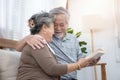 Elderly senior asian couple sitting on sofa reading book together at home.Retirement grandmother and grandfather spend time