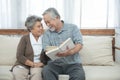 Elderly senior asian couple sitting on sofa reading book together at home.Retirement grandmother and grandfather spend time Royalty Free Stock Photo