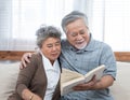 Elderly senior asian couple sitting on sofa reading book together at home.Retirement grandmother and grandfather spend time Royalty Free Stock Photo
