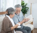 Elderly senior asian couple sitting on sofa reading book together at home.Retirement grandmother and grandfather spend time Royalty Free Stock Photo