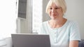 Elderly senior blond woman working on laptop computer at home. Remote freelance work on retirement Royalty Free Stock Photo