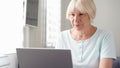 Elderly senior blond woman working on laptop computer at home. Remote freelance work on retirement Royalty Free Stock Photo