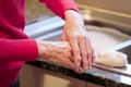 Elderly senior lady applying hand cream to old wrinkled cracked dry hands to moisturise for skin care