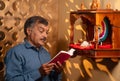 elderly senior man reading hymns from religious book in front of god near mandapam at home at morning - concept of Royalty Free Stock Photo