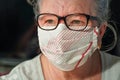 Elderly senior woman with glasses wearing hand made cotton mouth nose virus face mask. Coronavirus covid-19 outbreak prevention