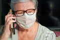 Elderly senior woman with glasses wearing hand made cotton mouth nose virus face mask, talking over her phone. Coronavirus covid Royalty Free Stock Photo