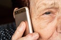 Elderly senior woman holding gold coloured phone next to her ear, closeup detail, only half face visible. Royalty Free Stock Photo