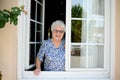 Elderly senior woman opening a window of her house and welcoming people at home Royalty Free Stock Photo