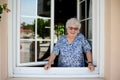 Elderly senior woman opening a window of her house and welcoming people at home Royalty Free Stock Photo