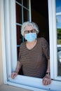 Elderly senior woman opening window of her house and welcoming people at home wearing a surgical mask to avoid covid19 and coron Royalty Free Stock Photo