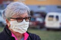 Elderly senior woman wearing home made cloth face mouth nose virus mask outside, blurred buildings and cars background. Can be