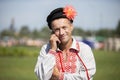 An elderly Slavic man in an embroidered shirt speaks on the phone.