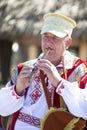 An elderly Slavic man in national dress plays the pipe.