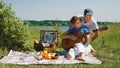 An elderly slender couple arranges a romantic picnic on the beach on a sunny summer day: a woman learns to play Royalty Free Stock Photo