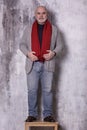 Elderly stylish bald gray-haired man stands on a wooden chair, vertical