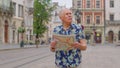 Elderly stylish tourist grandfather man walking along street looking for way using paper map in city