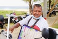 Elderly Thai man sells lottery tickets on the side of the road next to the beach