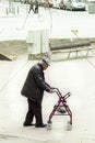 Elderly walking leaning on a small support cart