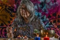 Elderly white-haired woman lightning an incense with colorful clothes