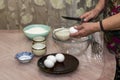 An elderly woman breaks an egg with a knife into a glass bowl for making pancake batter.Ingredients on the table-milk, salt, sugar Royalty Free Stock Photo