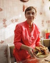 An elderly woman in bright clothes lays the table, lays out homemade cakes, pies on a plate,prepares to treat guests