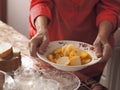 An elderly woman in brightly colored clothes sets the table, holds, and offers homemade diet potato soup as she treats guests.