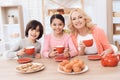 Elderly woman and cheerful grandson and granddaughter drink tea from red mugs in kitchen.