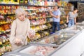 Mature woman choosing frozen food in supermarket. Young woman purchasing goods in grocery store