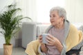 Elderly woman covered with blanket drinking tea at nursing home. Assisting senior people