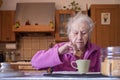 Elderly woman dips her cookie into a cup of latte during breakfast